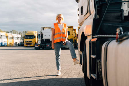 Caucasian middle-aged woman in front of yellow semi-truck vehicle on a parking lotの写真素材