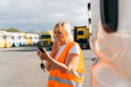 Caucasian middle-aged woman having a phone call in front of yellow semi-truck vehicle