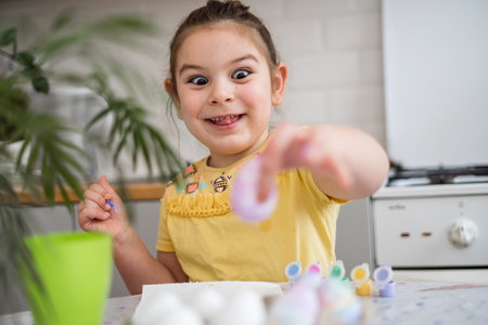 Child girl of preschool age painting Easter eggs at home kitchen. Easter spring traditions.の写真素材