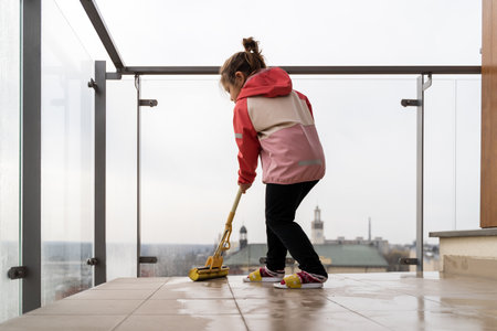Preschool age girl cleaning balcony floor with mop. Spring cleaning conceptの写真素材