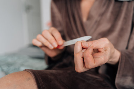 mature woman hands close-up using nail file for manicure at homeの写真素材