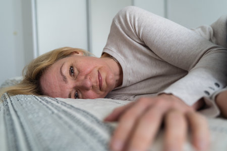 Mature woman curled lying on the bed at home top view. Depression, mental health, abuse problemの写真素材