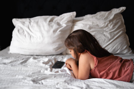 5 years old girl watching cartoons on mobile phone on the bed. royal luxury interiorの写真素材