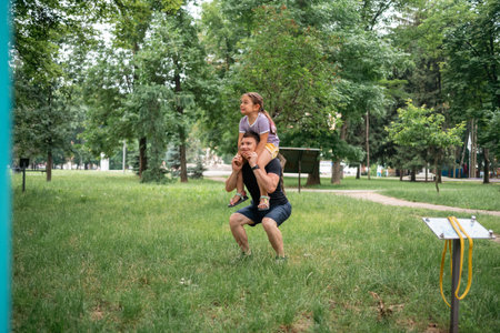 father doing squats with child daughter on the shoulders. active workout with family, healthy...