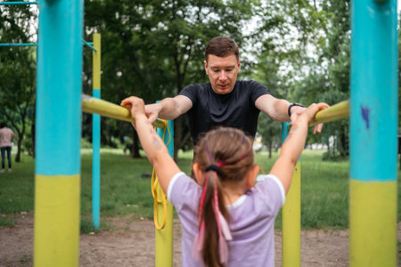 Father with child girl doing pull-ups on workout outdoor area. Healthy active lifestyle, happy...