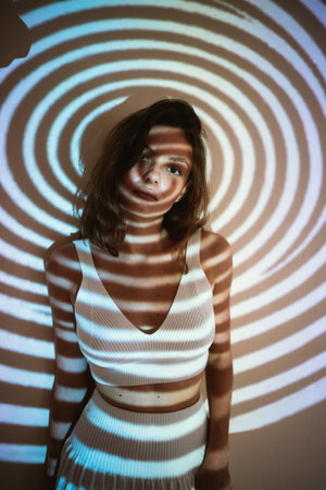young adult woman or teenager girl in trendy outfit in dark room with projected geometrical illusion on her, aesthetic vibeの写真素材