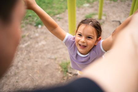 Young child daughter playing with father on the workout outdoors gym. Happy emotions. Healthy family lifestyleの写真素材