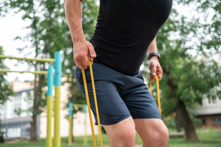 Middle age man doing strength exercises with resistance bands outdoors in park
