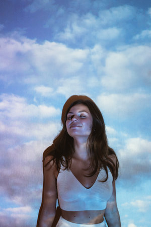 Young adult beautiful z-gen woman with clouds image projected on her with projectorの写真素材