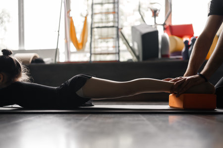 Close up of unrecognisable coach hands holding child girl legs during stretching strength exercise during dance or gymnastics trainingの写真素材