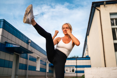 Adult beautiful blonde woman doing box kicks exercises workout outdoors, boxing fighting class. Healthy lifestyle, self defence skillsの写真素材
