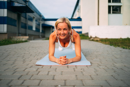 Middle age musical build beautiful woman doing plant on the yoga mat outdoors in urban area park. Core exercise workout.の写真素材