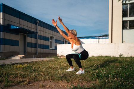 Beautiful blonde woman doing glutes exercises with resistance bands outdoors. Healthy sporty lifestyle, outdoors workoutの写真素材