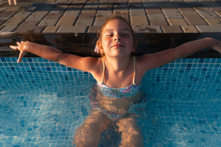 Child girl relaxing at the pool on a sunny hot summer day. Poolside resort concept, heat wave, climate changeの写真素材