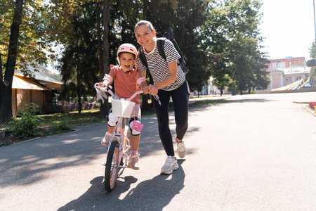 Mother learning child girl to ride a bike in the park in the summer. Happy quality family time together. Empowering, essential physical skills for kids.の写真素材