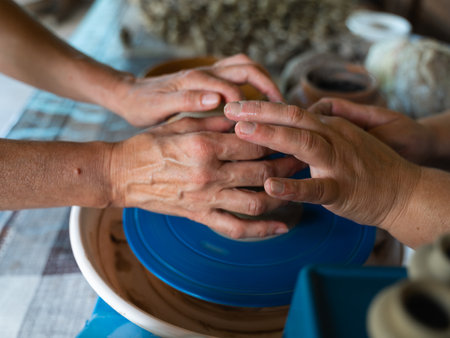 Close up of hands of two women pottering. One learning another on a potters wheel. modelling a ceramic vessel by hands, traditional Ukrainian hand craftの写真素材