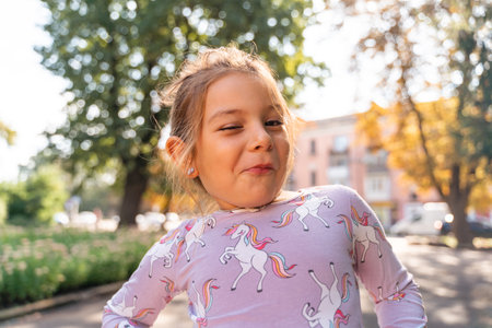Portrait of a funny caucasian 5-6 years old girl making a face outdoors in a city. Close-up portrait...