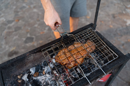 Caucasian close-up hands cooking beef steak on the grill net on coal bbq outdoors. Back yard bbq party in summer or autumnの写真素材