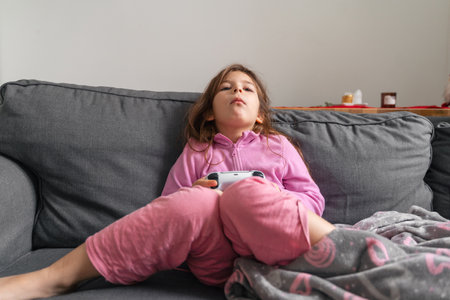 Child girl bored on the sofa at home playing video gamesの写真素材