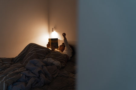 Adult reading a book in bed with child at nightの写真素材