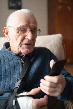 Senior with injured arm in sling browsing smartphone.