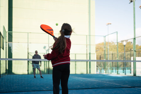 A focused young girl practices her paddle tennis skills on a vibrant blue court on a clear dayの写真素材
