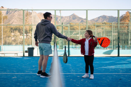 A smiling girl playing paddle tennis with her father, both showing excitement and joy in an outdoor courtの写真素材