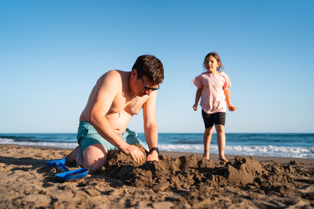 Bonding over beach play, a father and daughter focus intently on constructing a grand sandcastle togetherの写真素材