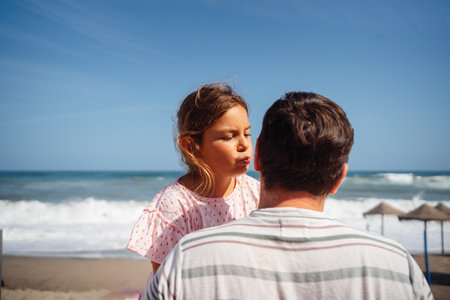 A father holds his young daughter by the ocean, sharing a peaceful and tender moment outdoorsの写真素材