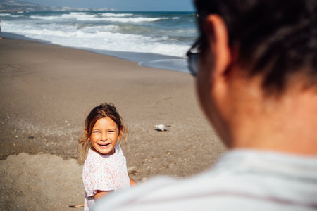 A father spends quality time with his daughter by the ocean, sharing a relaxed and joyful day at the beachの写真素材