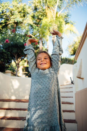 A smiling young girl enjoys a sunny day outdoors, standing near flowers and plantsの写真素材