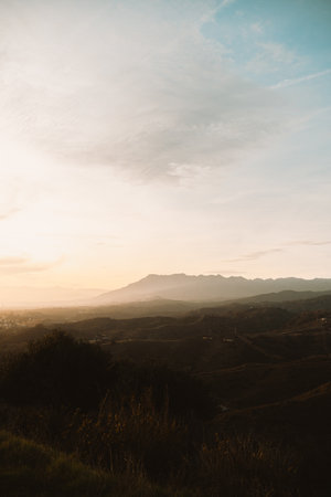 Softly lit hills and distant mountains under a golden sunset, creating a peaceful natural landscapeの写真素材