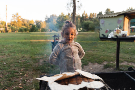 A girl places flatbread on a barbecue grill, participating in outdoor cooking during a family picnicの写真素材
