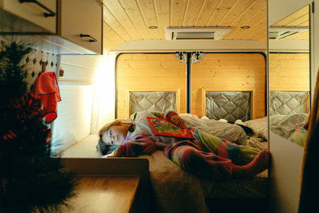 Caucasian female child relaxing in cozy camper bed with book and christmas decorationsの写真素材