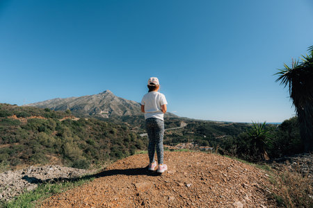 Young caucasian girl enjoying scenic mountain landscape under blue sky, slow living off grid free childhoodの写真素材
