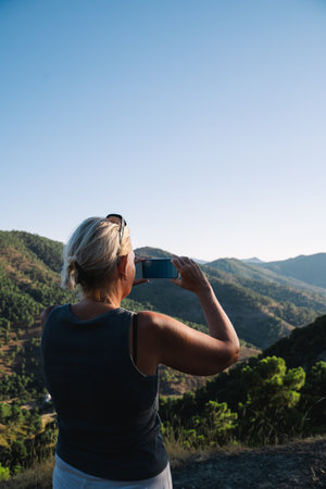 Woman standing on a hilltop in Andalusia, Malaga province, using her smartphone to photograph the...