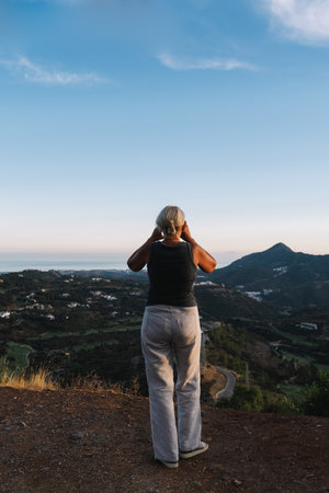 Woman standing on a hilltop in Andalusia, Malaga province, using her smartphone to photograph the...