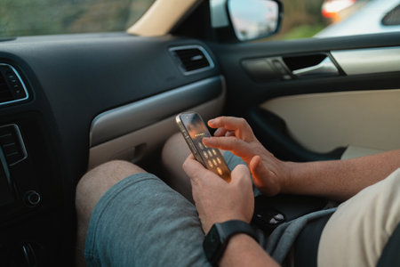 Closeup of a man sitting in a car passenger seat, using a smartphone while resting on his lap