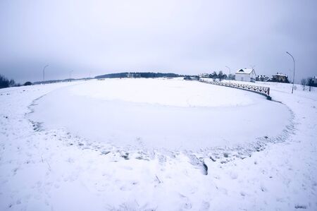 Ice and snow on round pond. Winter landscape.