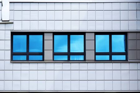 Facade of modern building. Reflection of blue sky in windows glass.の写真素材