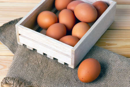 Raw brown eggs in wooden box and on canvas fabric on wooden table. Selective focus.の写真素材