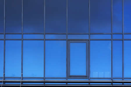 Windows on facade of modern building. Reflection of sky in windows glass. Abstract architectural blue background.の写真素材
