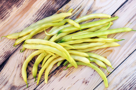 Pods of yellow green beans on wooden table. Top view.