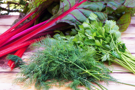 Fresh green dill, parsley and green leaves of chard with red stalks on wooden table. Selective...