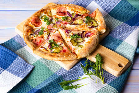 Bacon Pizza with pickled cucumbers, red onion and arugula on wooden cutting board.