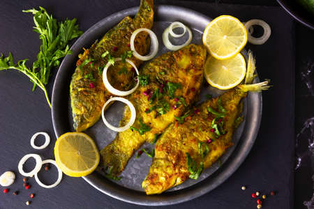 Fried Freshwater Fish with Lemon and Onions in a Plate on Black Slate Cutting Board. Bream, Carp and...