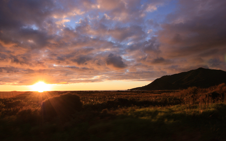 Sun setting behind the sea and lighting fields, New Zealandの写真素材