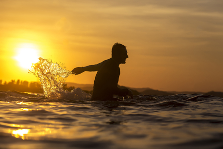 Surfer waiting in the line up for a wave at sunrise or sunsetの写真素材