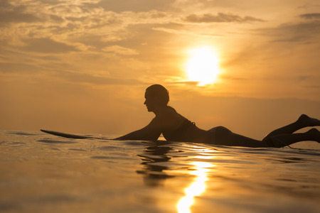 Surfer girl waiting in the line up for a wave at sunrise or sunsetの写真素材