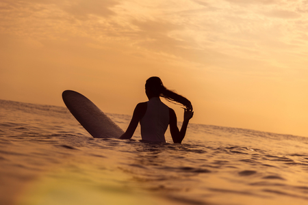 Surfer girl waiting in the line up for a wave at sunrise or sunsetの写真素材